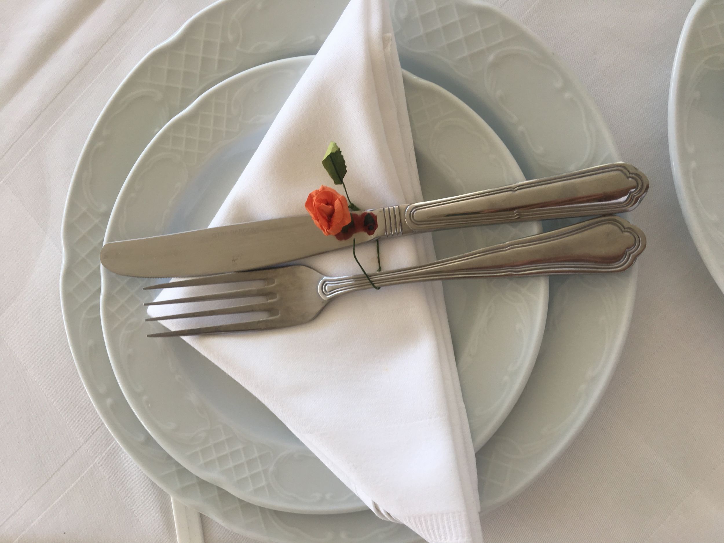 
Elegant table setting with whit plates, folded napkin and cutlery tied with a small orange flower