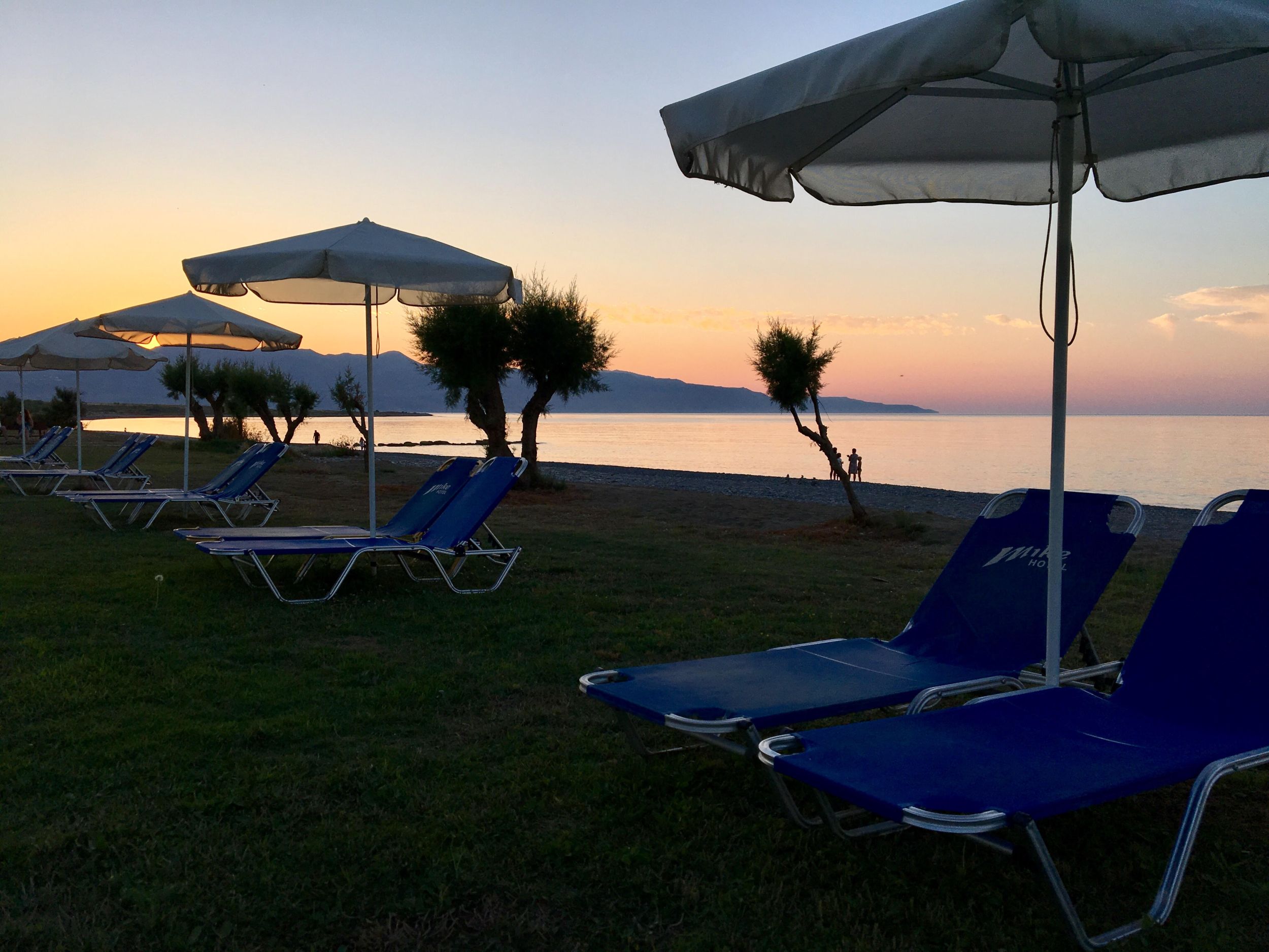 
Sunset over Maleme Beach with blue loungers and white umbrellas by the shoreline