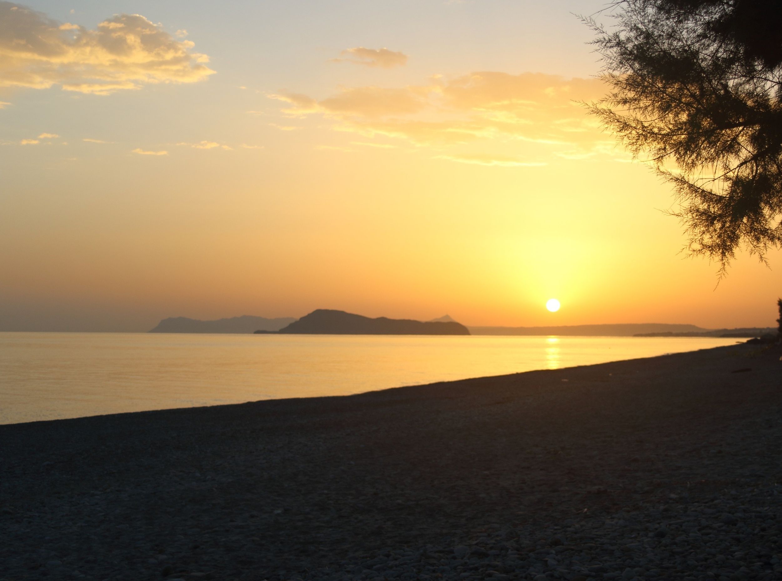
Golden sunrise over Maleme Beach with calm water and distant islands in view