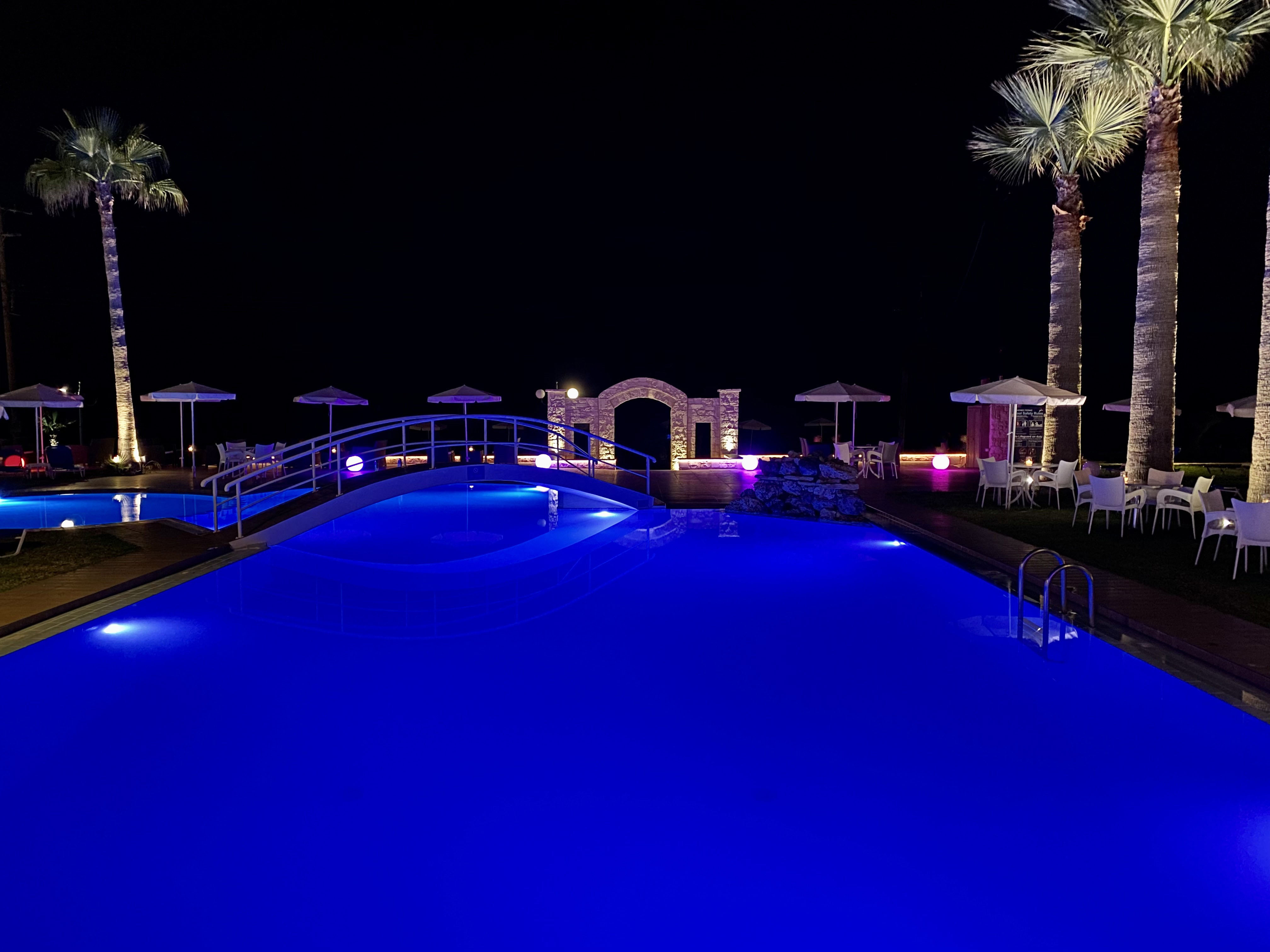 
Night view of the illuminated pool with palm trees and seating areas by the beach in Maleme