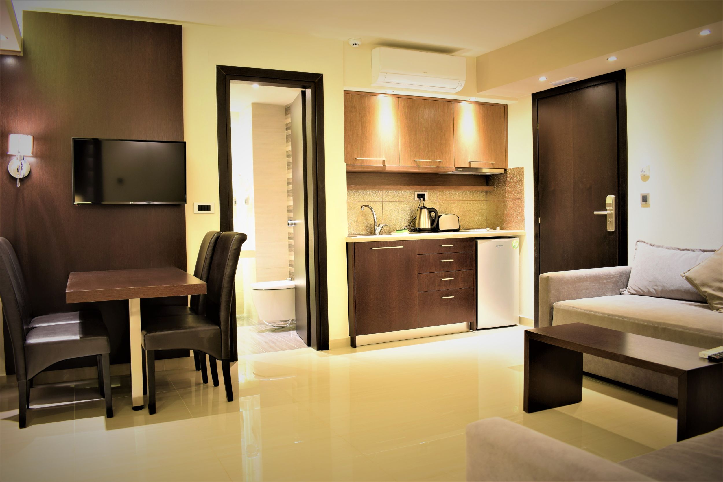 
Modern apartment with warm lighting featuring a kitchenette, dining area with TV and a sofa with a coffee table