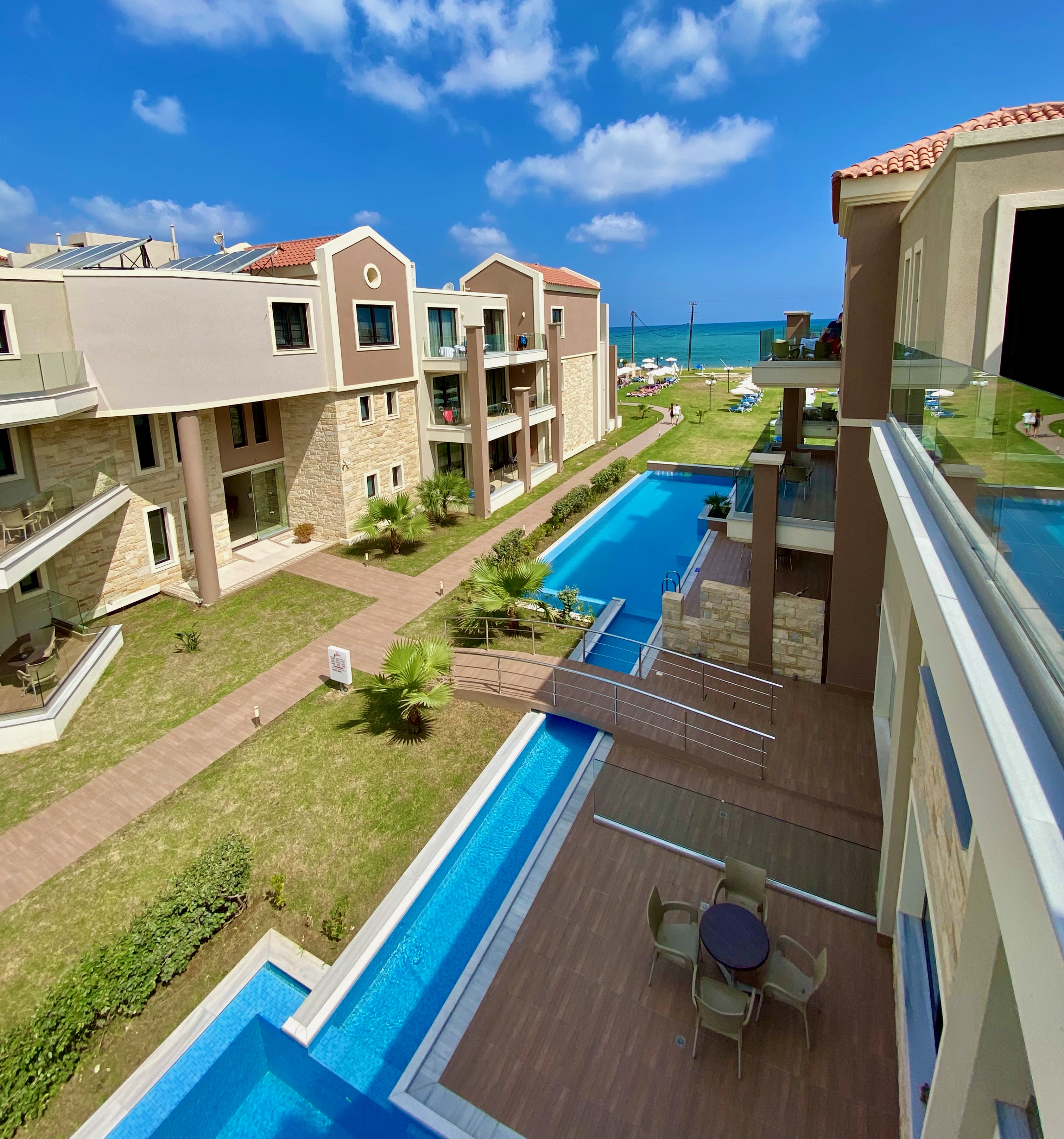 
Pool between the hotel buildings with a bridge, green lawn and the beach visible in the background