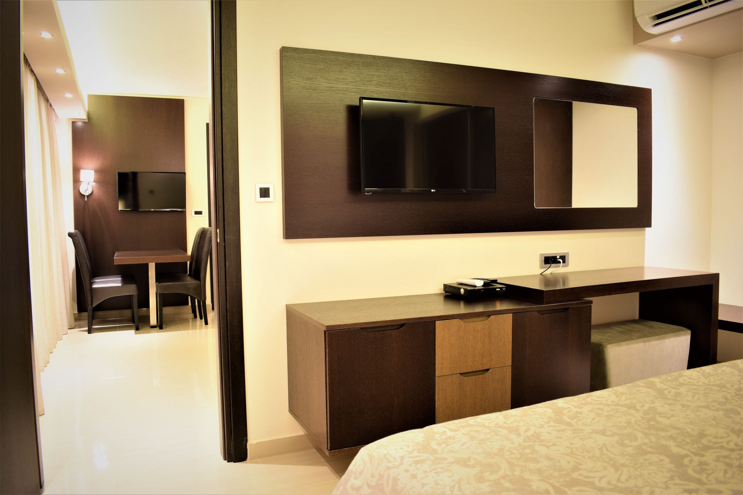 
Modern hotel room with wall-mounted TV, wooden desk and a view into the dining area in Mike Hotel