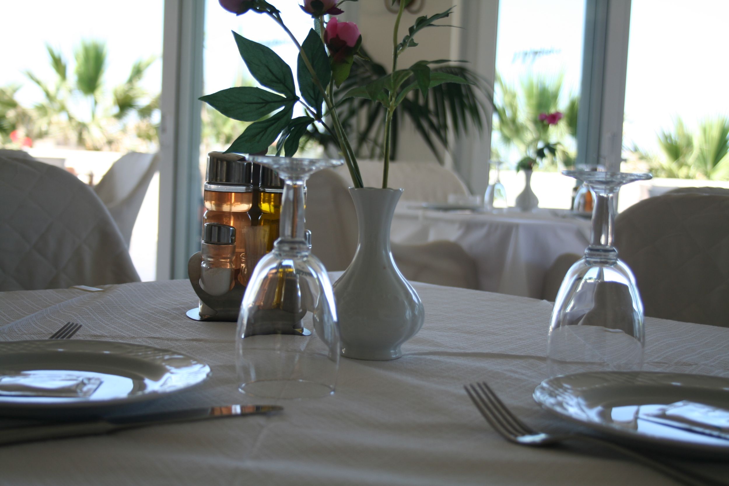 
Elegant restaurant table wth white linens, glassware and a small flower vase at Mike Hotel Apartments